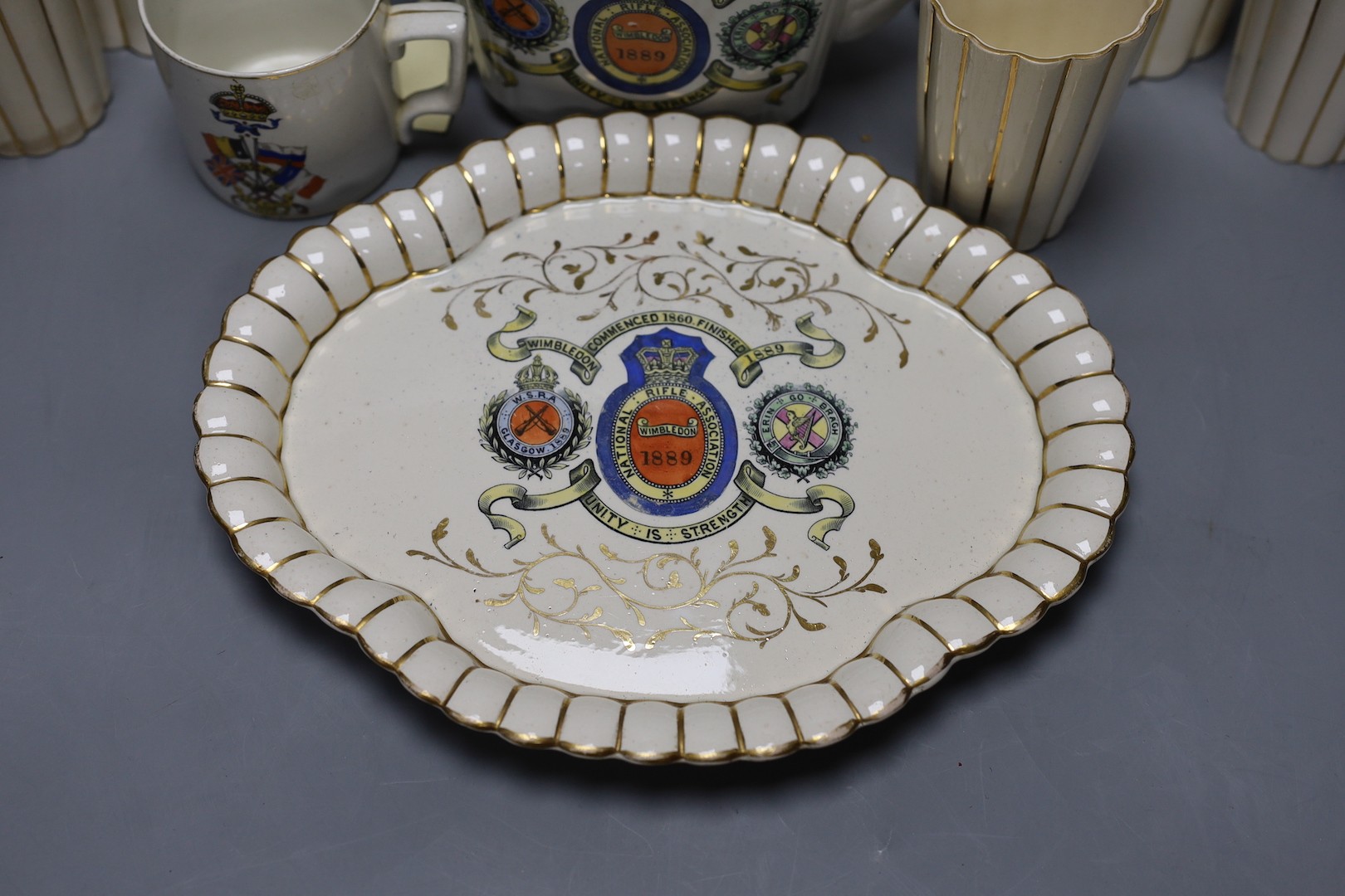 National Rifle Association Wimbledon 1889 - A group of Staffordshire commemorative pottery, including two water jugs, 18 cm high, and three matching beakers, a teapot and cover, a tray, together with a WW1 mug